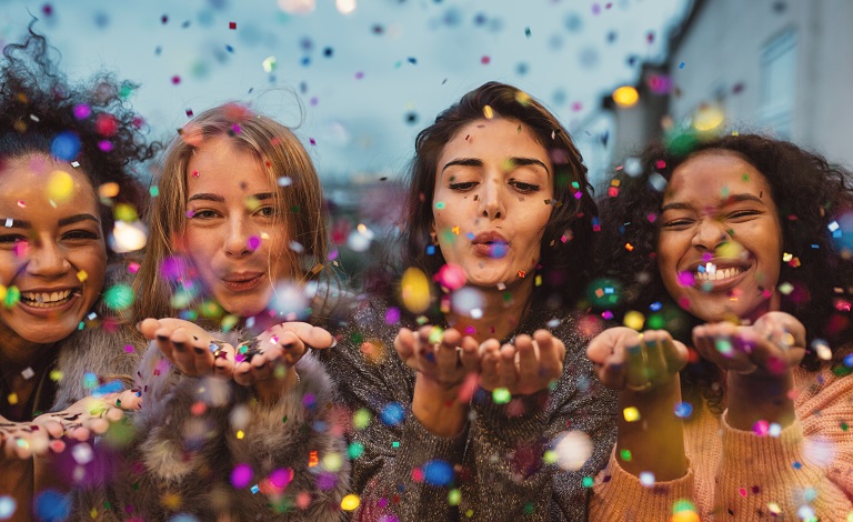 Four women blow sparkles and confetti.