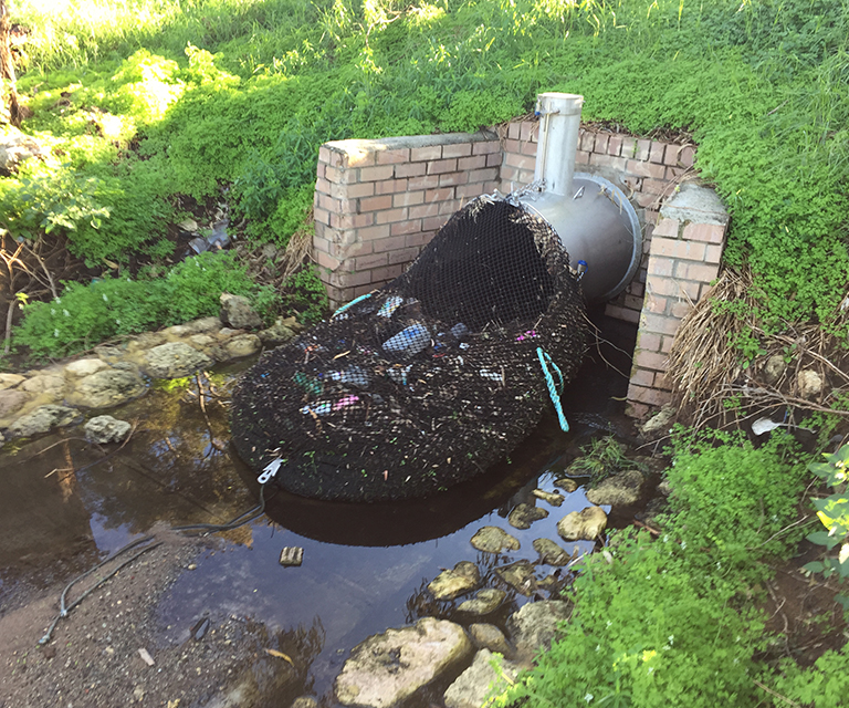 A drainage net filled with rubbish covers a pipe.