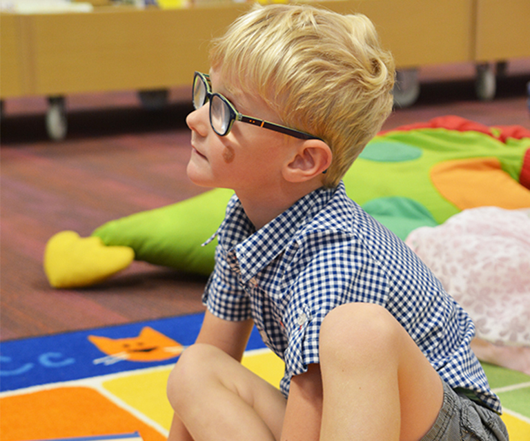 A young boy sits on a colourful rug.