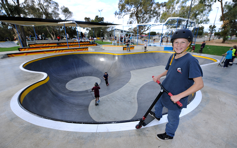 A boy on a scooter stands at the edge of the skatepark.