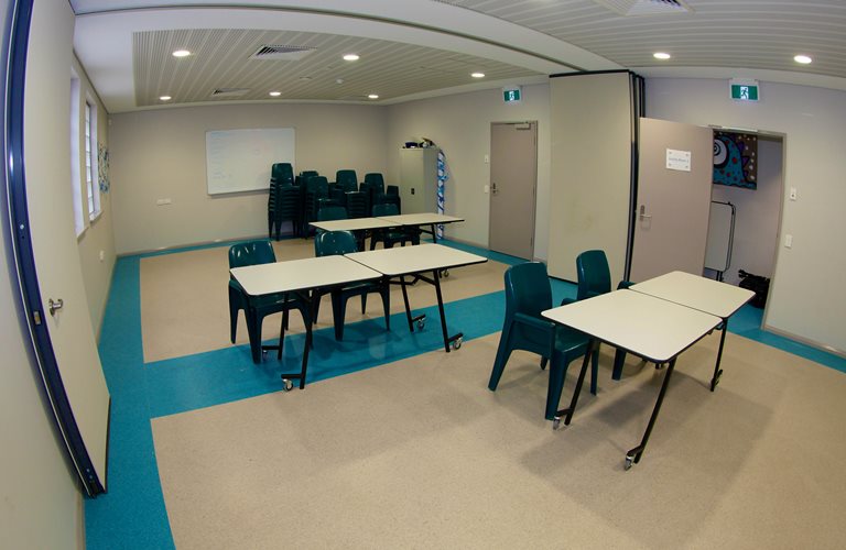 An activity room at Zone Youth Space, with six desks and a stack of chairs.