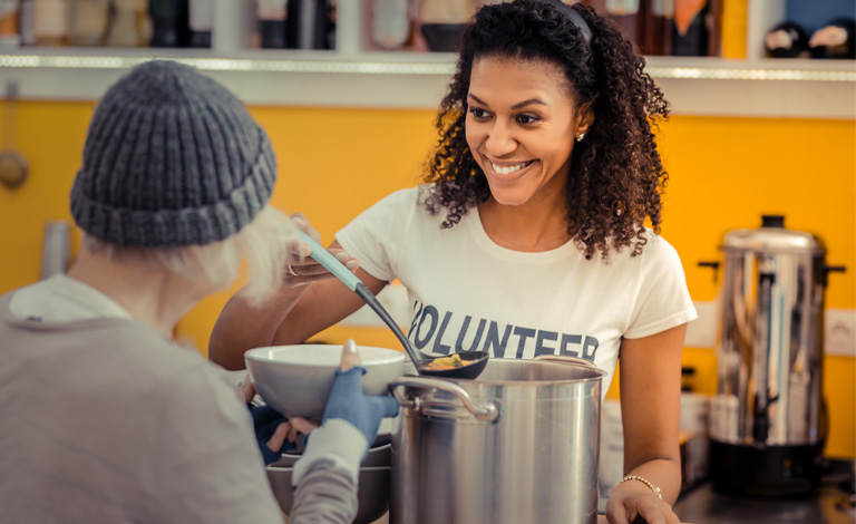 A volunteer serves a person soup.