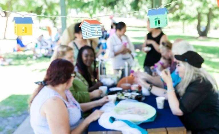 A group of people sit at a picnic table in a public park. 