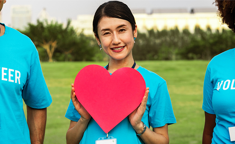 A woman smiles and holds a red heart symbol.