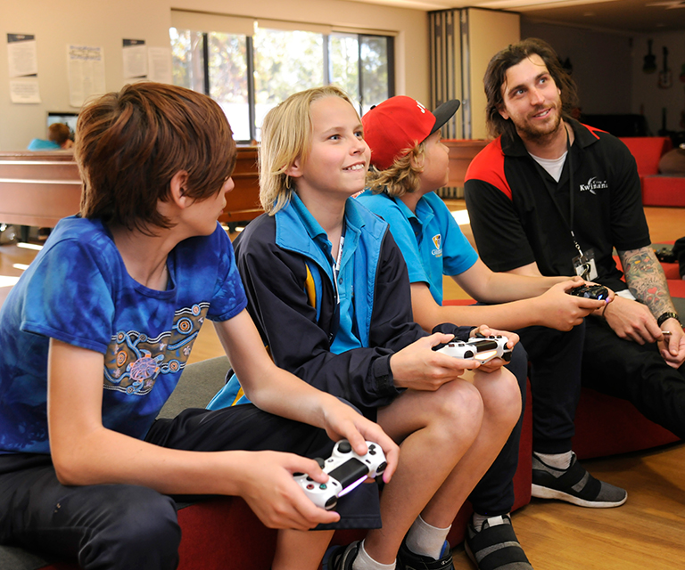 A staff member watches as boys play a video game.