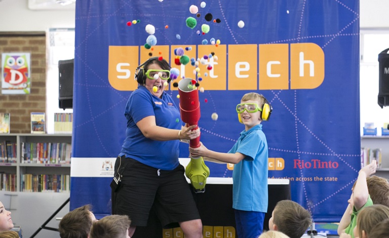 A Scitech staff member and a child hold a tube, which is shooting pom poms. 