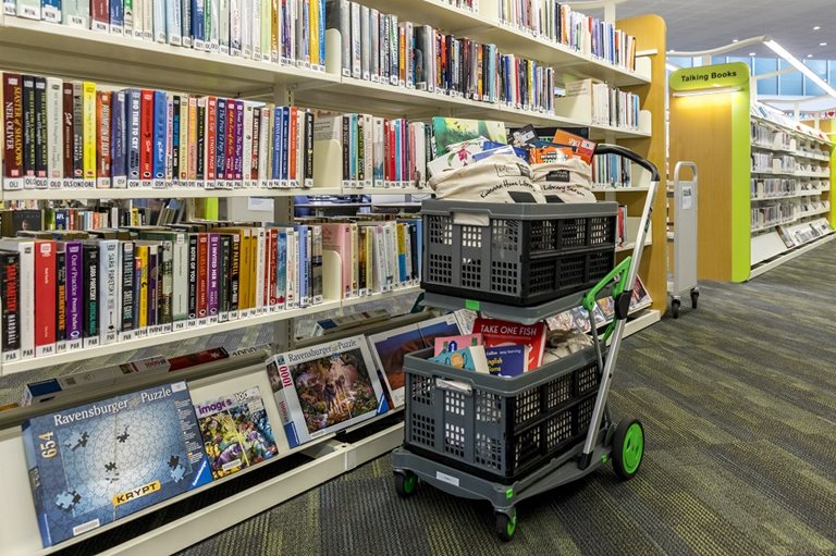 A trolley filled with books between the shelves.